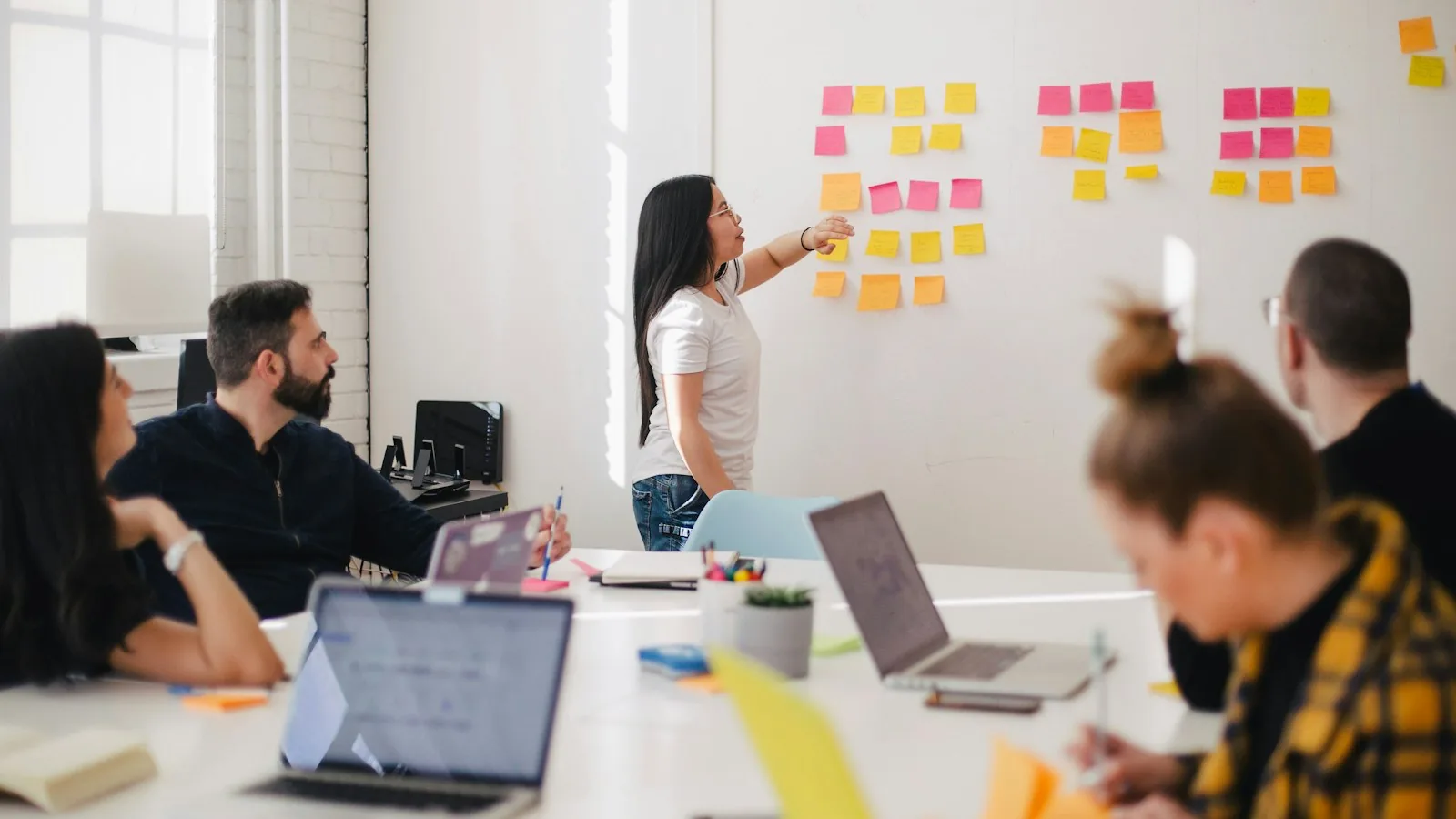 A team in a meeting room, one person placing sticky notes on a glass wall